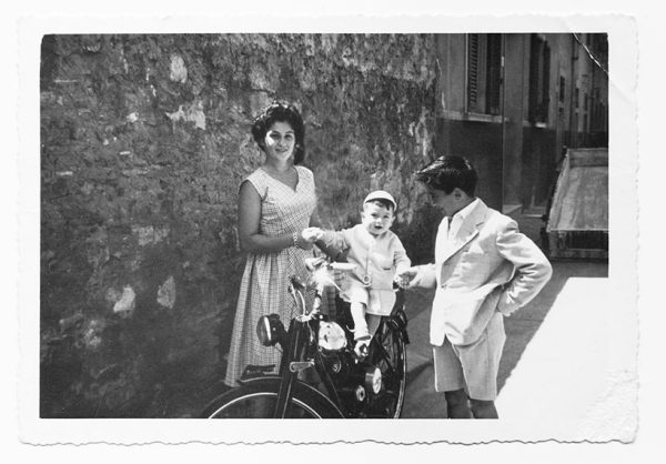 Black and white photo of Italian family, with baby on moped. 