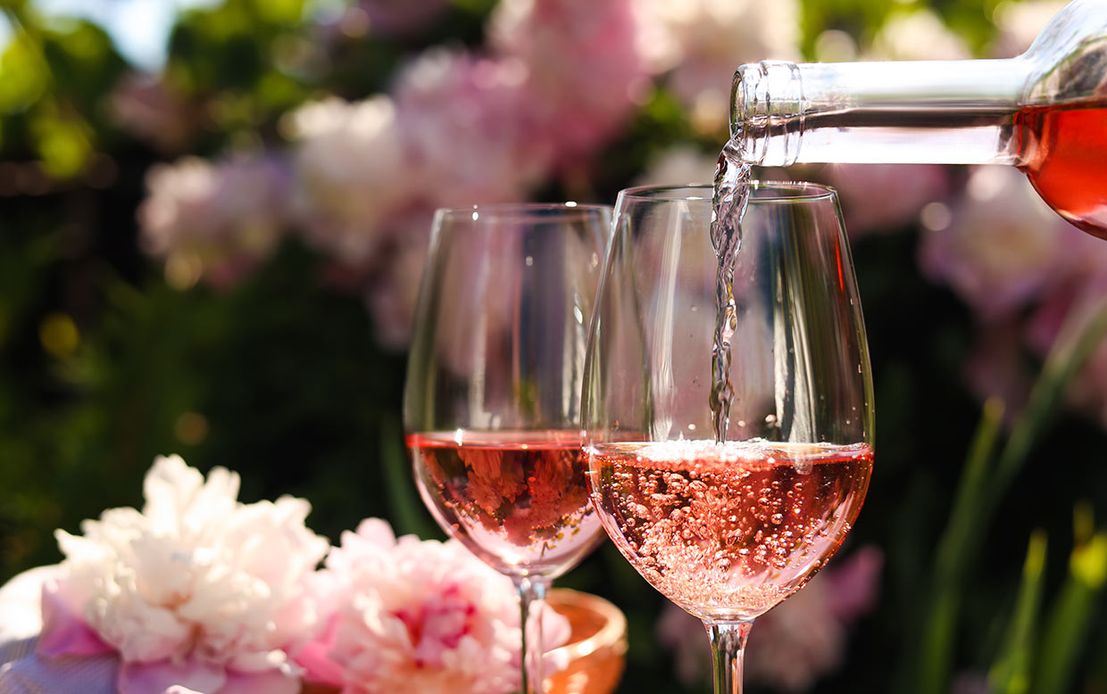 Pouring rose wine into glass in garden, closeup