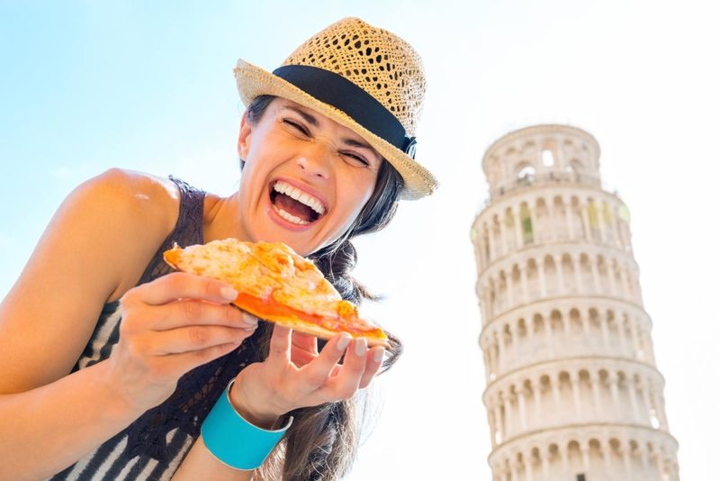 Laughing woman tourist holding slice of pizza in Pisa