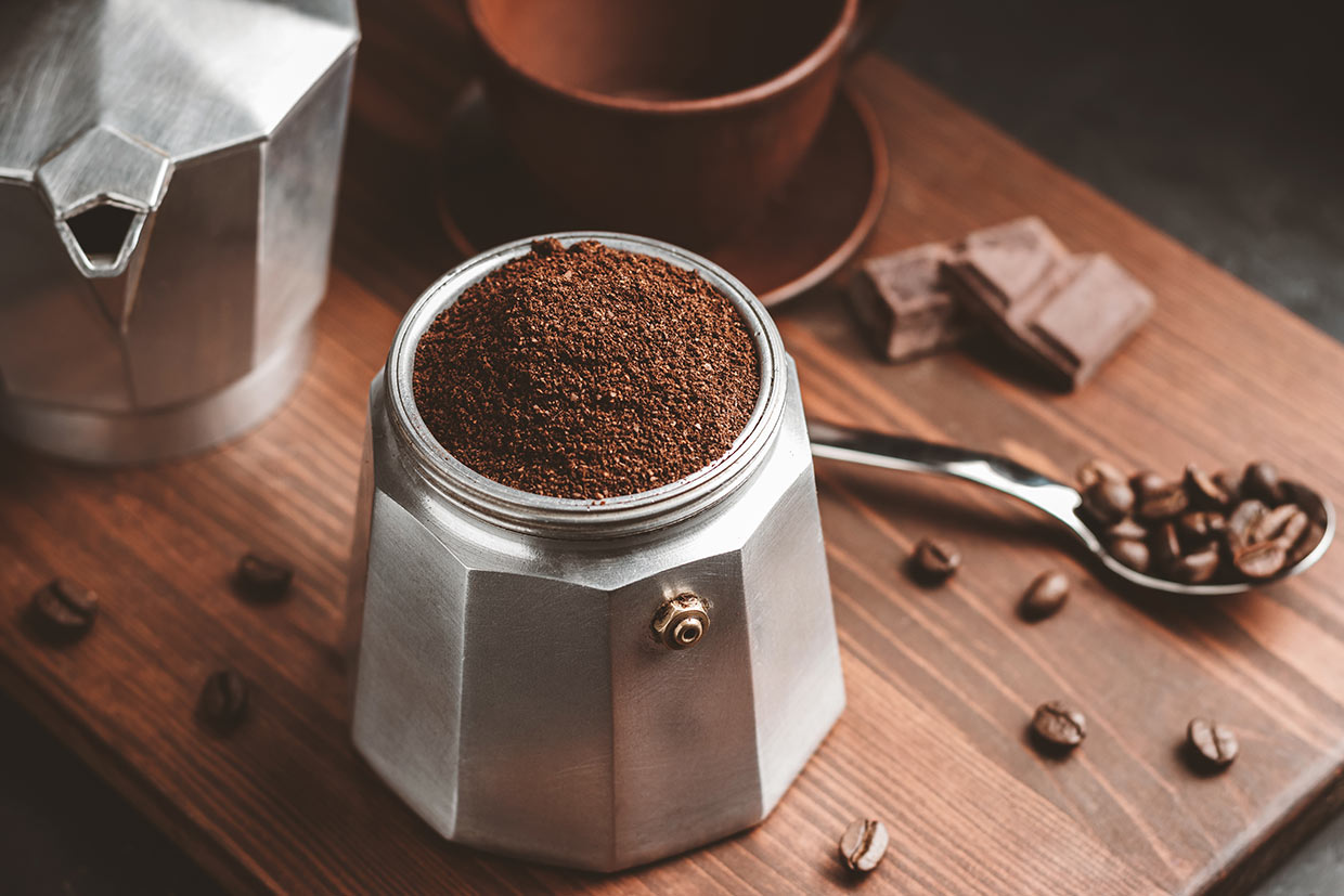 Moka coffee pot filled with brown ground coffee on dark wooden board, prepare to brewing Italian espresso