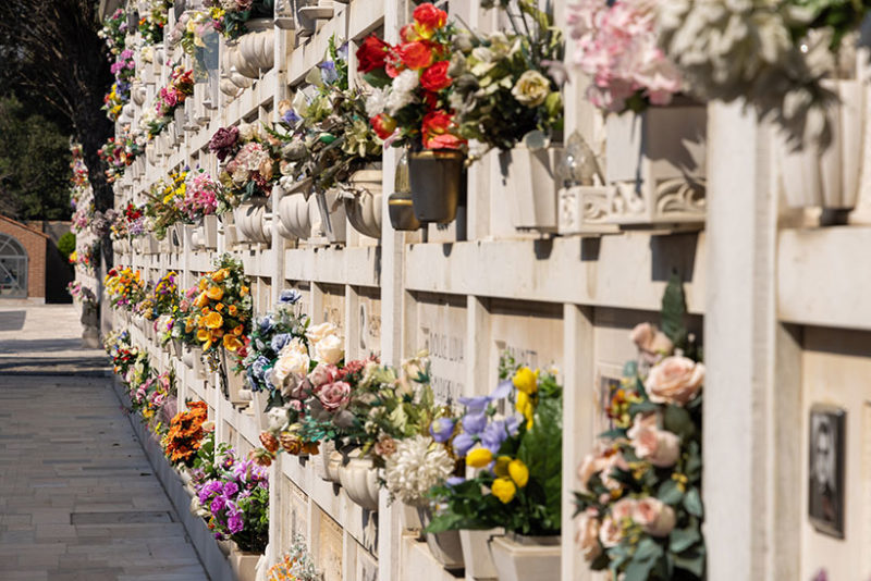 Italian wall cemetery with tombstones and artificial flowers on a sunny summer day in Venice